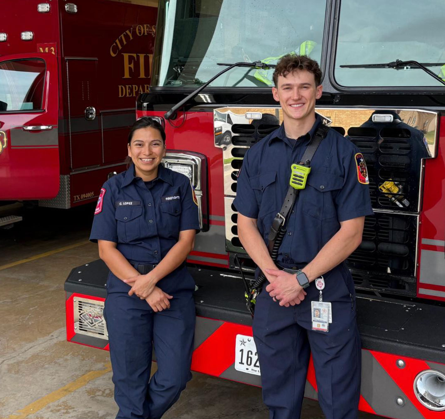 Female and male firefighters smiling by the fire truck
